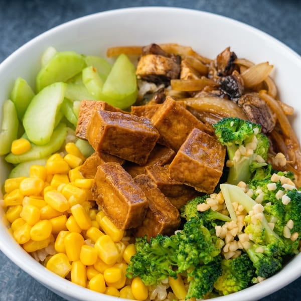 Close-up of a vegan bowl with tofu, corn, broccoli, celery, and onions.