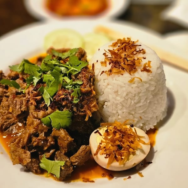 Braised beef with cilantro, white rice, and a hard-boiled egg on a white plate.