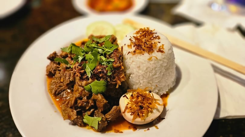Braised beef with cilantro, white rice, and a hard-boiled egg on a white plate.