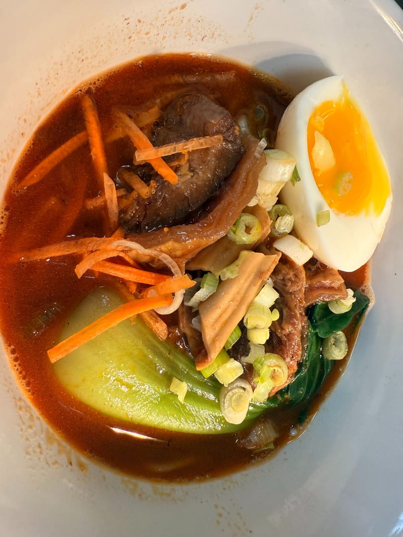 A close-up of ramen with pork, bok choy, carrots, scallions, and a soft-boiled egg.