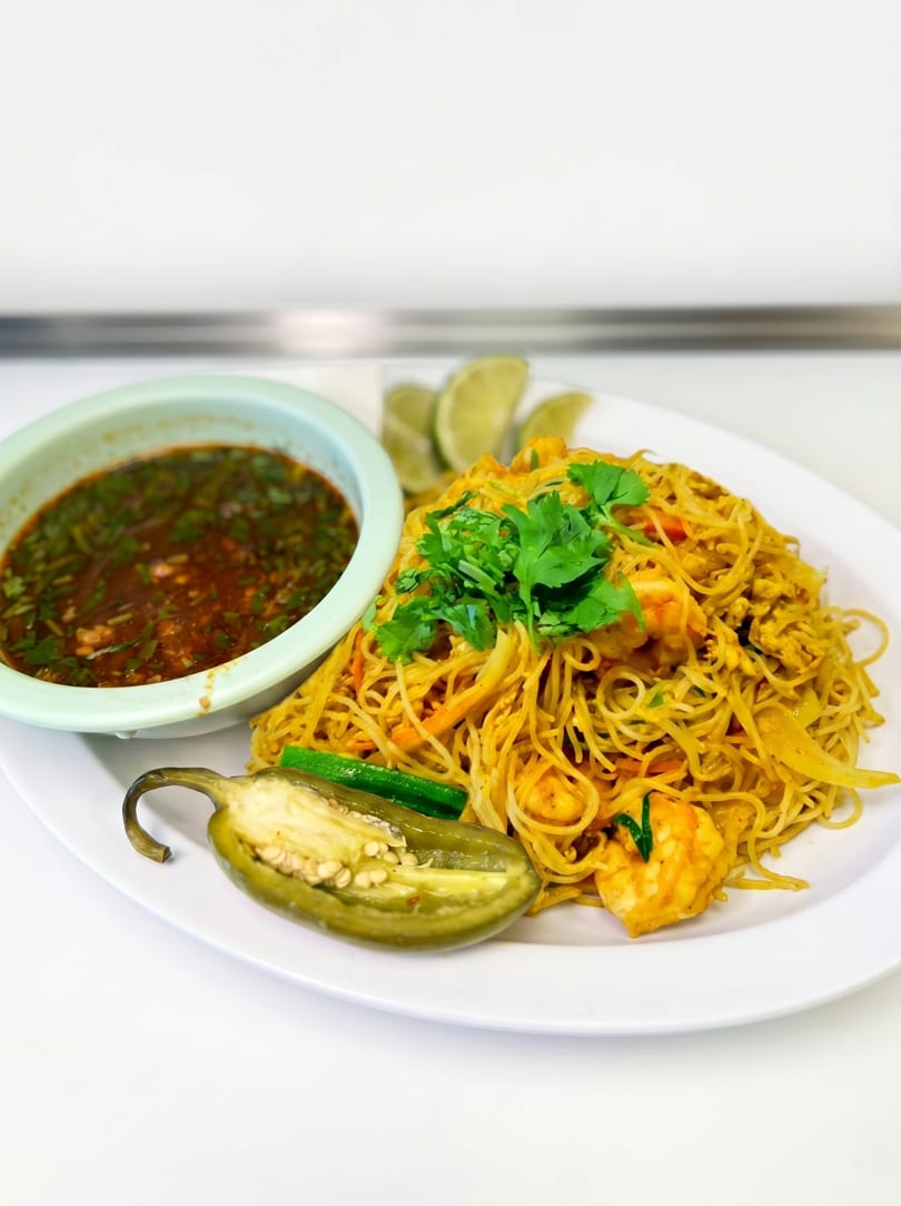 Shrimp Pad See Ew noodles with a side of dipping sauce, lime wedges, and a halved jalapeño.